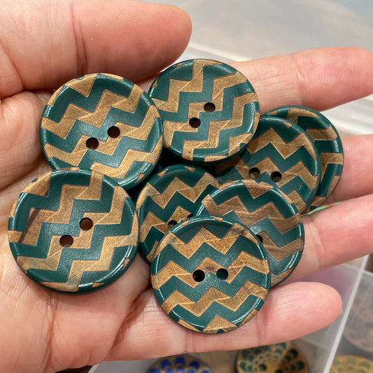Hand holding decorative buttons with a box of more buttons in the background