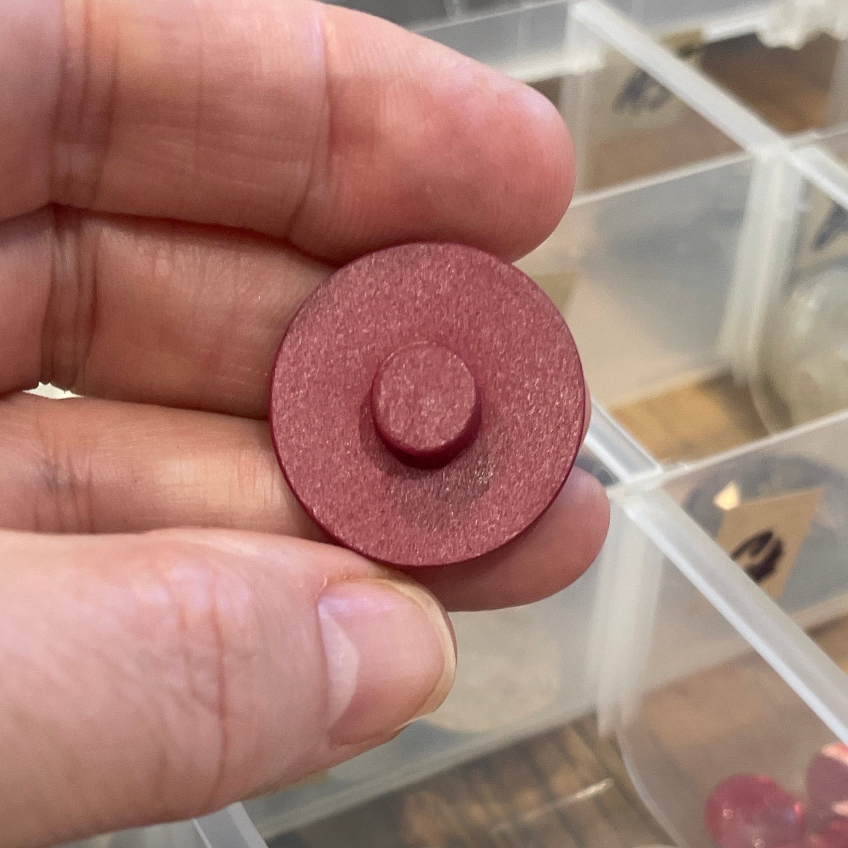 Hand holding a button with a clear container of buttons in the background