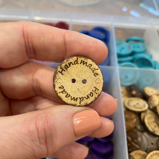 Handmade button held by a hand with a blurred background of button assortment