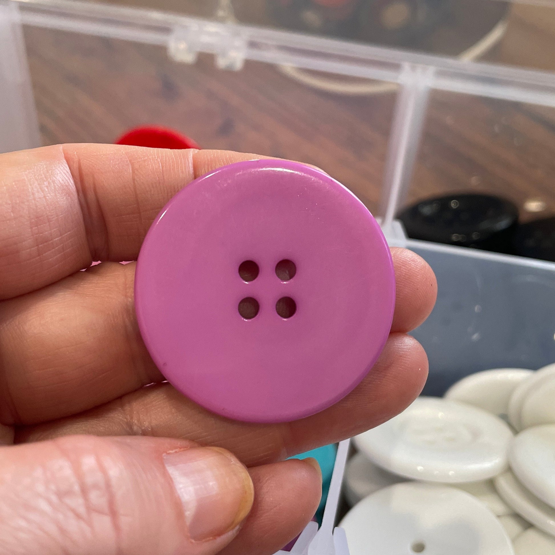 Hand holding a pink button with a blurred background of buttons and containers