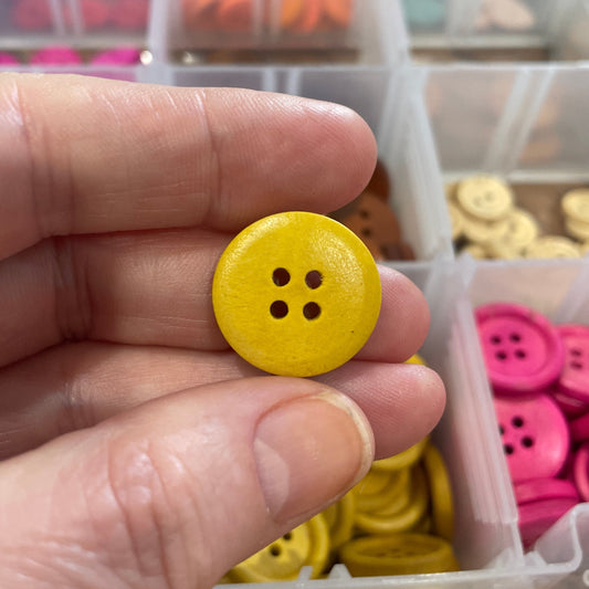 Yellow button held in a hand with a container of buttons in the background