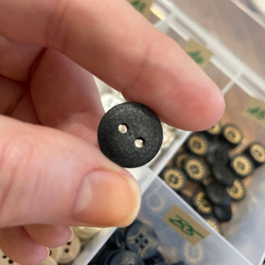 Hand holding a black button with a container of buttons in the background