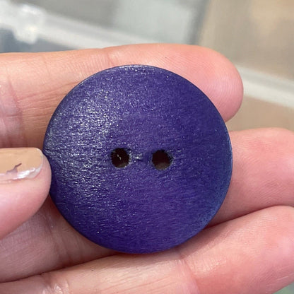 Purple button held in a hand with a container of buttons in the background