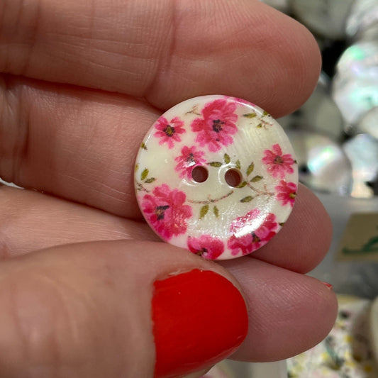 Hand holding a floral button with a blurred background of more buttons.