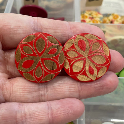 Hand holding two red floral-patterned buttons with a background of a button organizer.