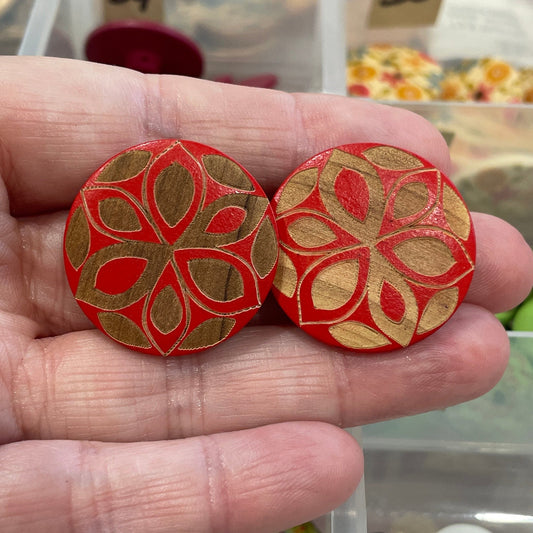 Hand holding two red floral-patterned buttons with a background of a button organizer.