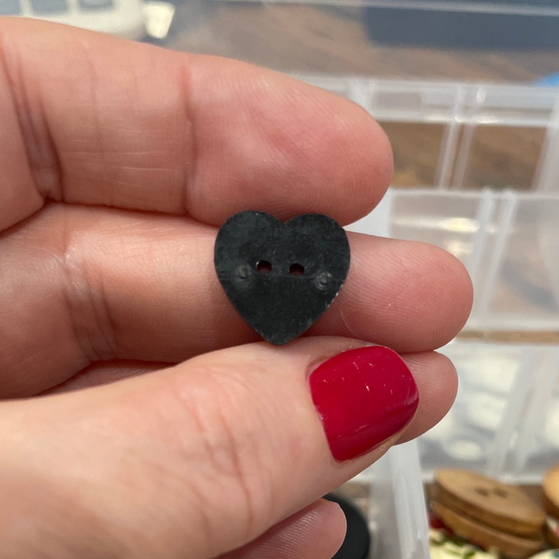 Hand holding a black button with a container of assorted buttons in the background