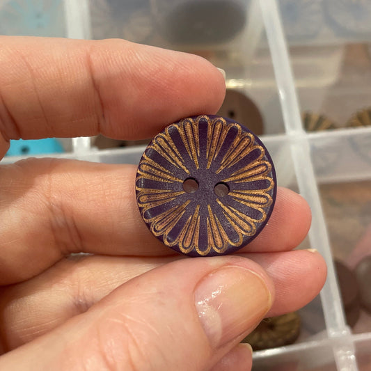 Hand holding a decorative button with a background of a button collection in a box.