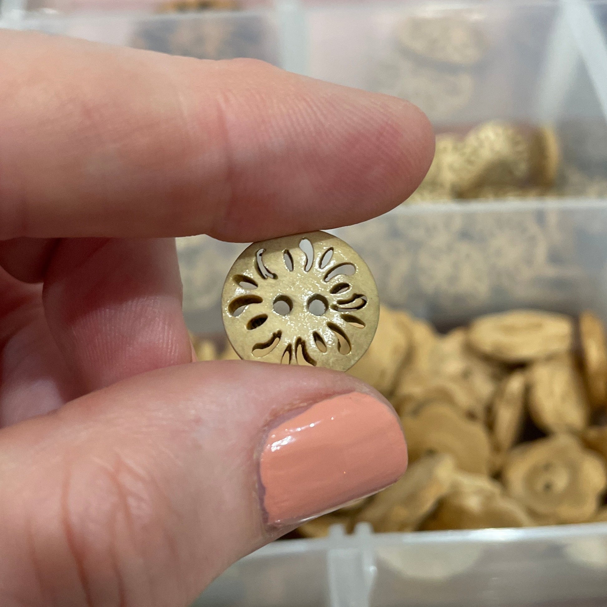 Hand holding a gold button with a clear container of buttons in the background
