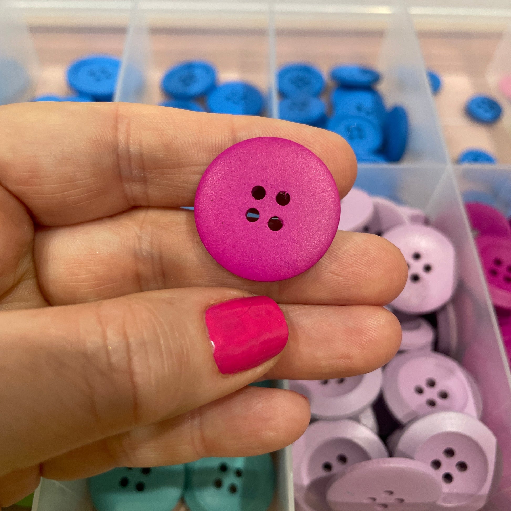 Hand holding a pink button with a container of buttons in the background