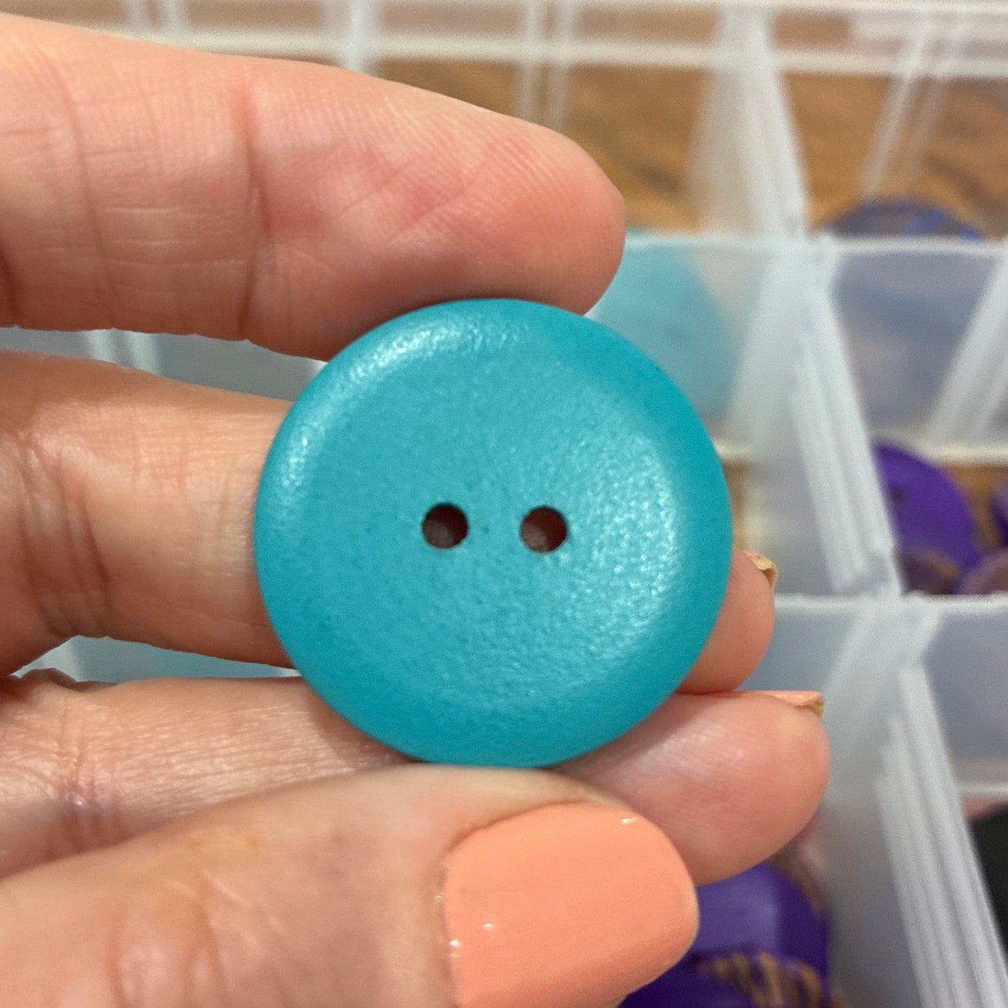 Hand holding a blue button with a blurred background of a storage box with various items.