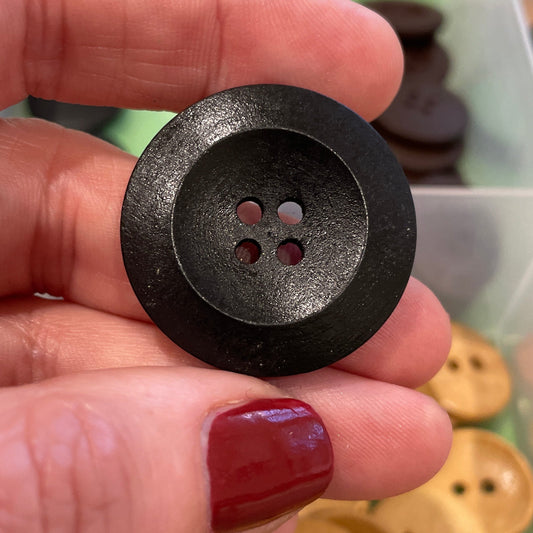 Hand holding a black button with a container of buttons in the background