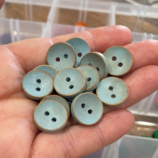 Hand holding a small collection of round buttons with a container of buttons in the background.