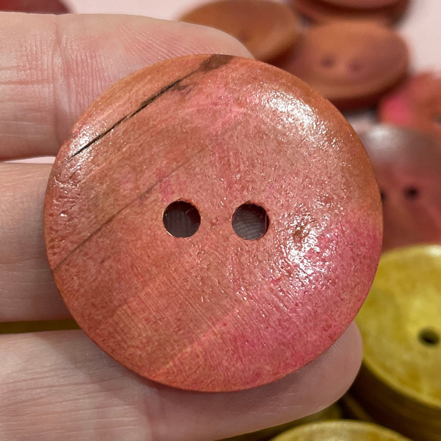 Close-up of a hand holding a pink button with other buttons in the background.