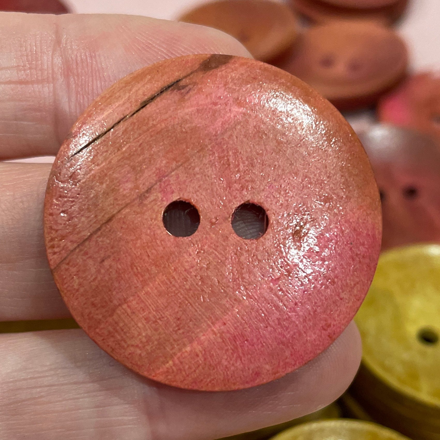 Close-up of a hand holding a pink button with other buttons in the background.