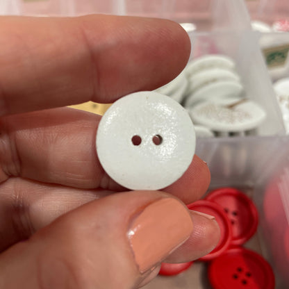 White button held between fingers with a container of buttons in the background