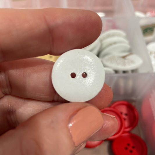 White button held between fingers with a container of buttons in the background