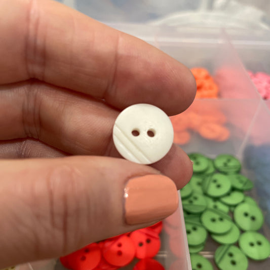 White button held by a hand with a container of colorful buttons in the background