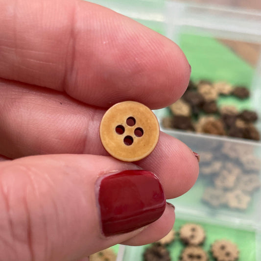 Hand holding a wooden button with a container of similar buttons in the background