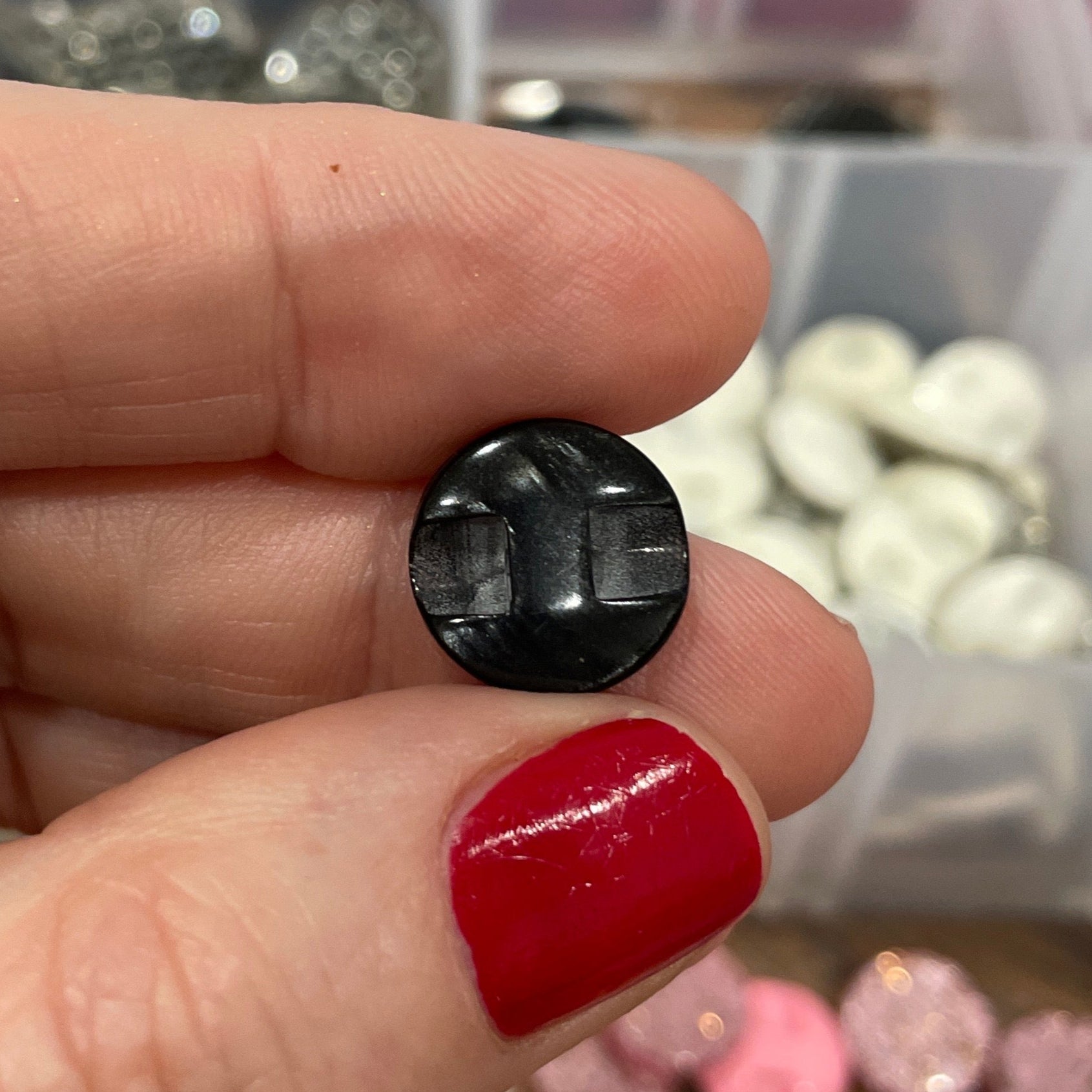 Black button held between fingers with a container of buttons in the background