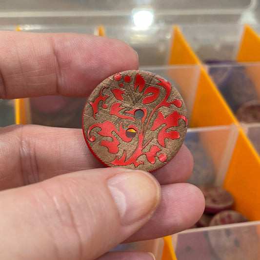Hand holding a decorative button with intricate patterns in front of a button organizer.