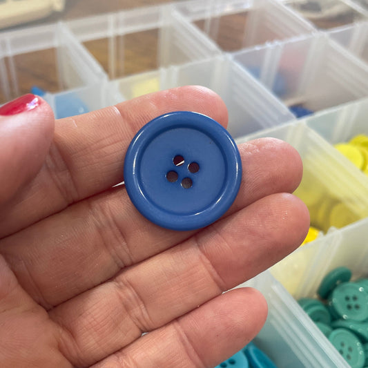 Blue button held in a hand with a container of buttons in the background