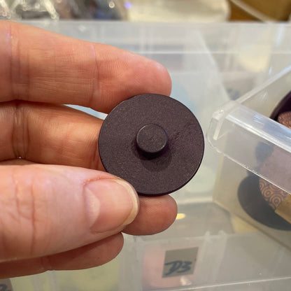 Hand holding a round brown button with a container of buttons in the background