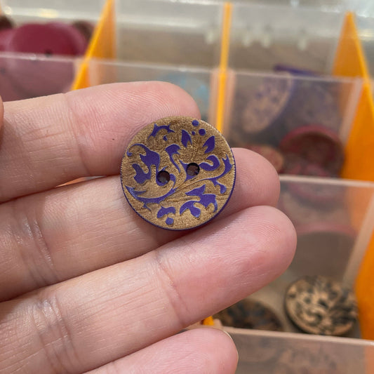 Close-up of a hand holding a decorative button with a colorful pattern, against a background of a button collection.