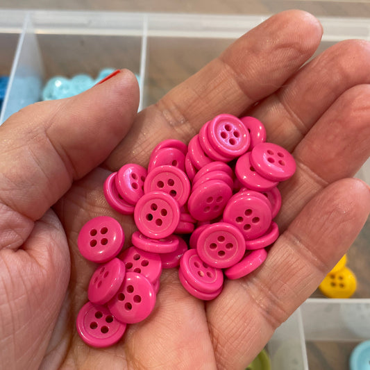 Hand holding pink buttons with a blurred background of more buttons.