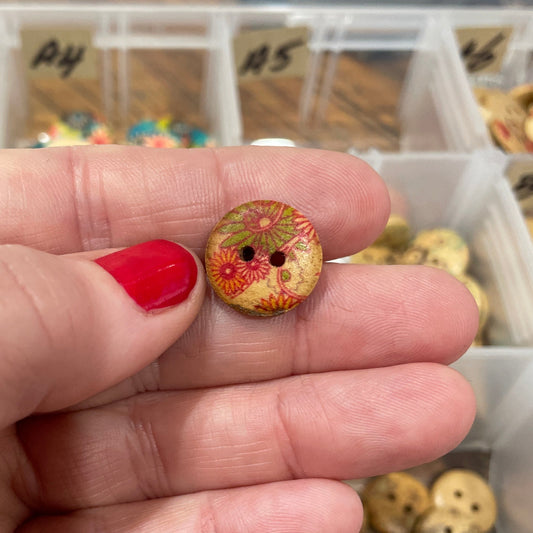 Hand holding a decorative button with a background of a button organizer.