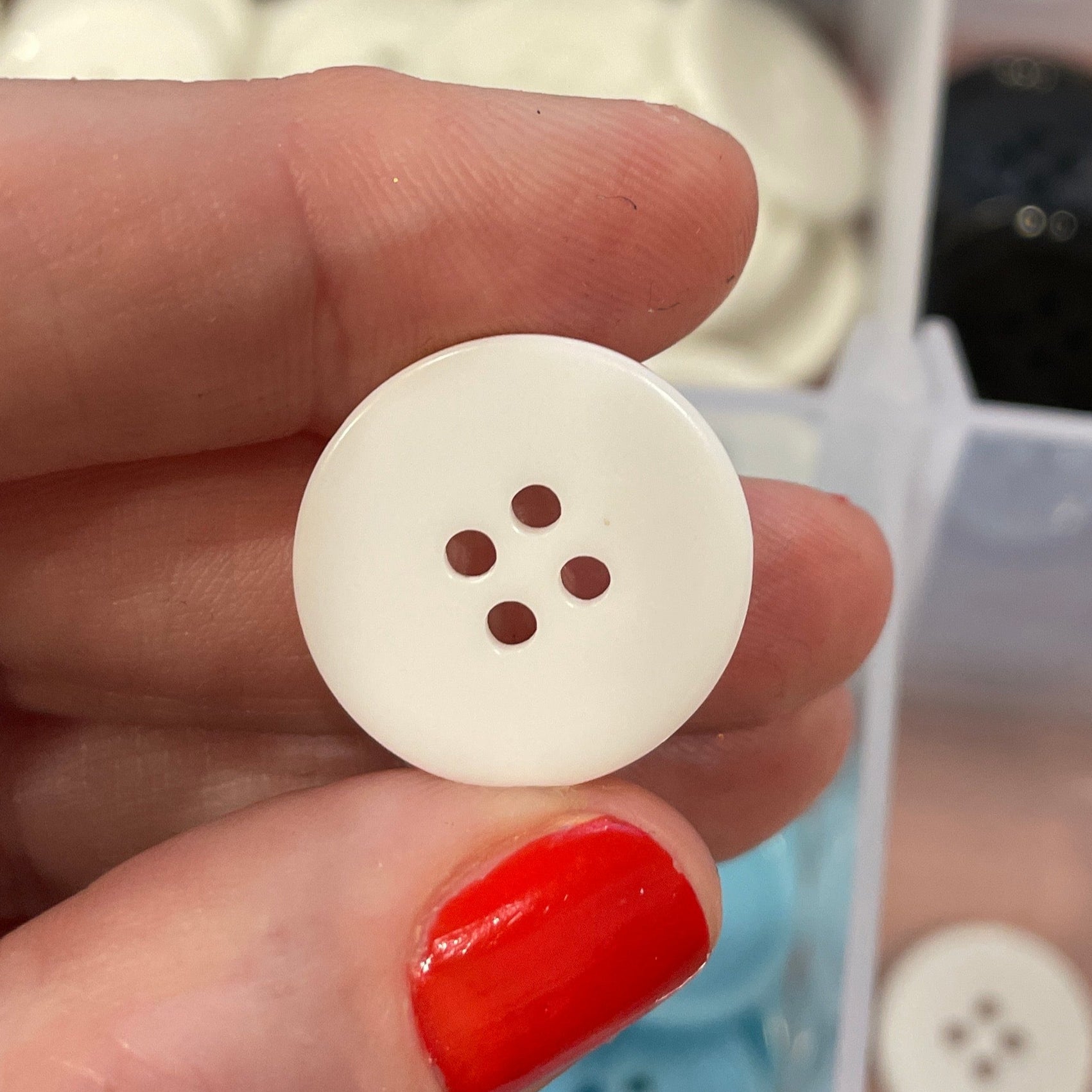 White button held by a hand with a blurred container of buttons in the background
