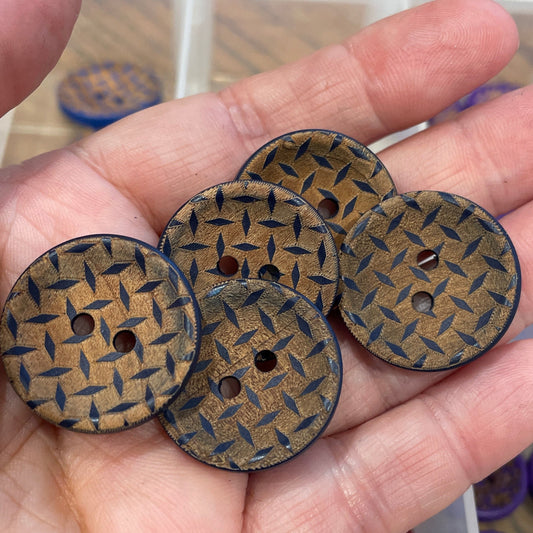 Hand holding four wooden buttons with a pattern, with a container of buttons in the background.