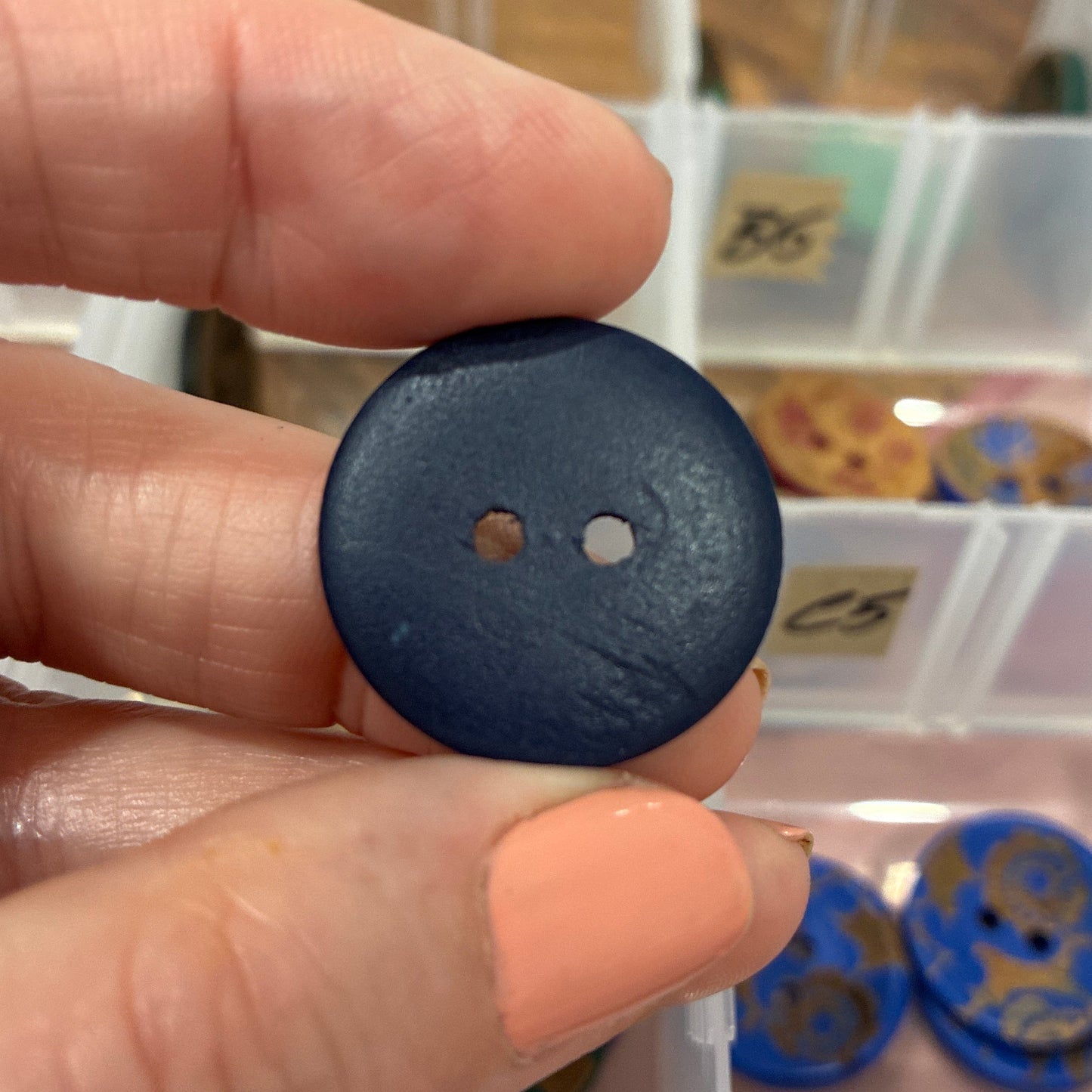 Hand holding a blue button with a clear plastic organizer in the background