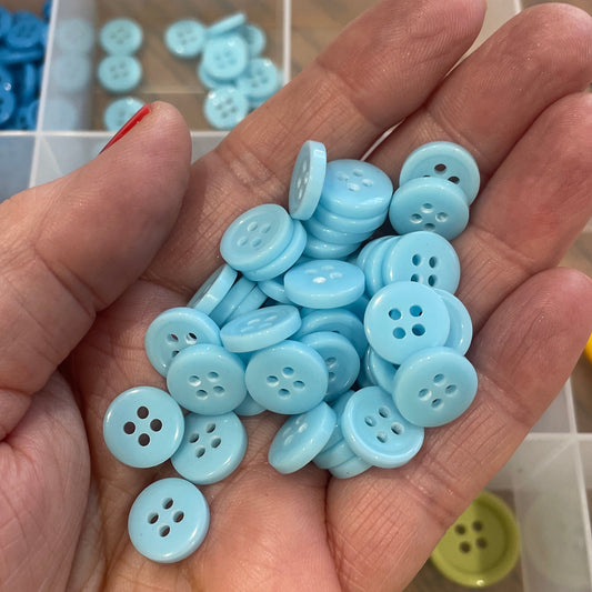 Hand holding blue buttons with a clear container of buttons in the background