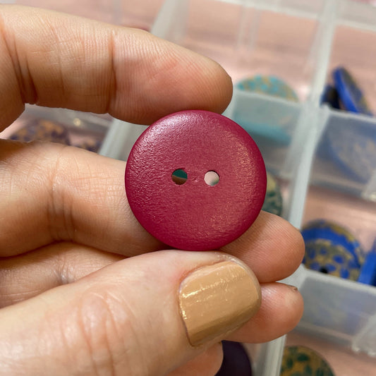 Hand holding a red button with a clear container of buttons in the background