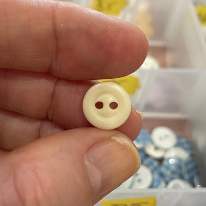 Hand holding a beige button with two holes in front of a container of buttons.
