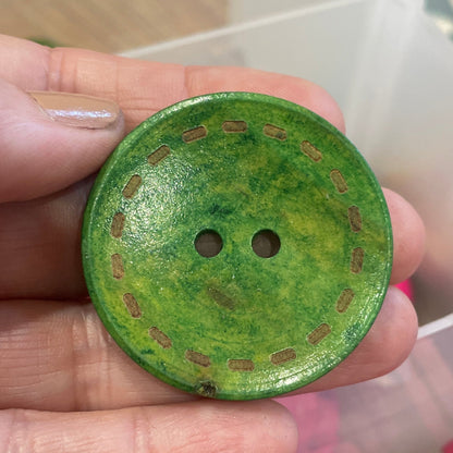 Green button held in a hand with pink buttons in the background