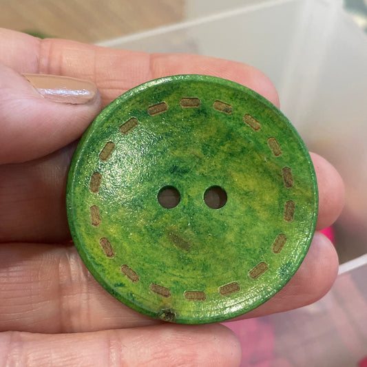 Green button held in a hand with pink buttons in the background