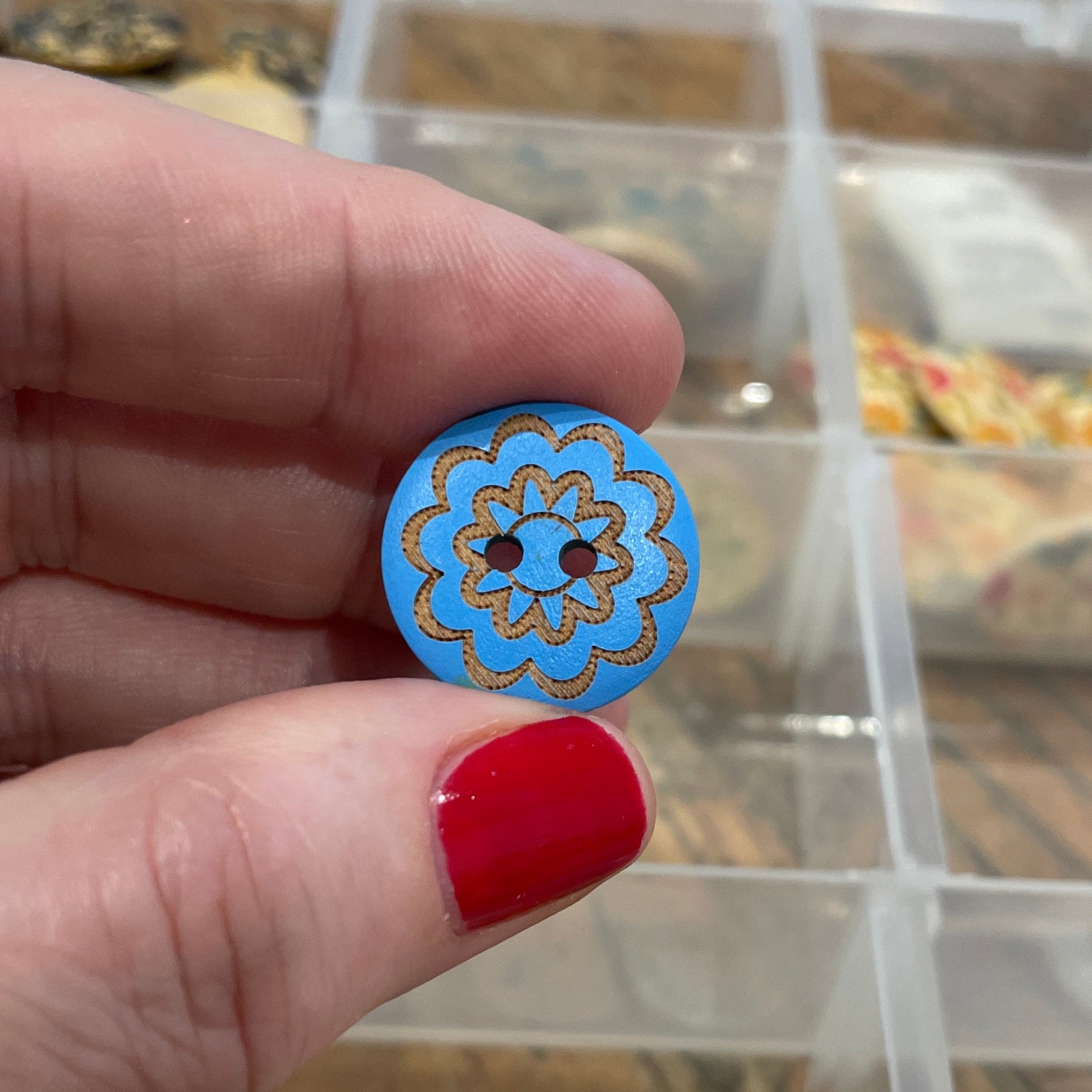 Hand holding a blue decorative button with a clear container of buttons in the background