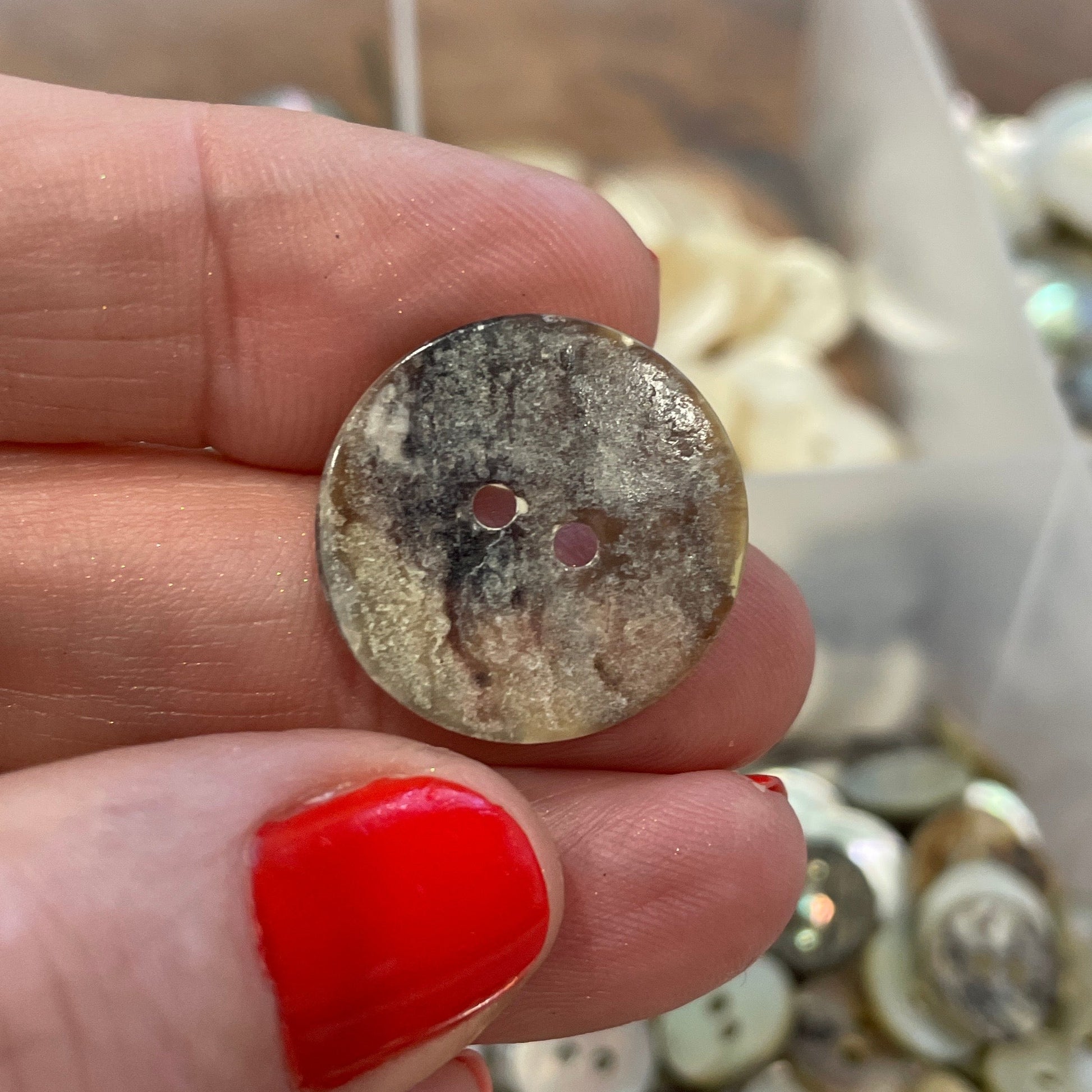 Hand holding a button with a container of buttons in the background