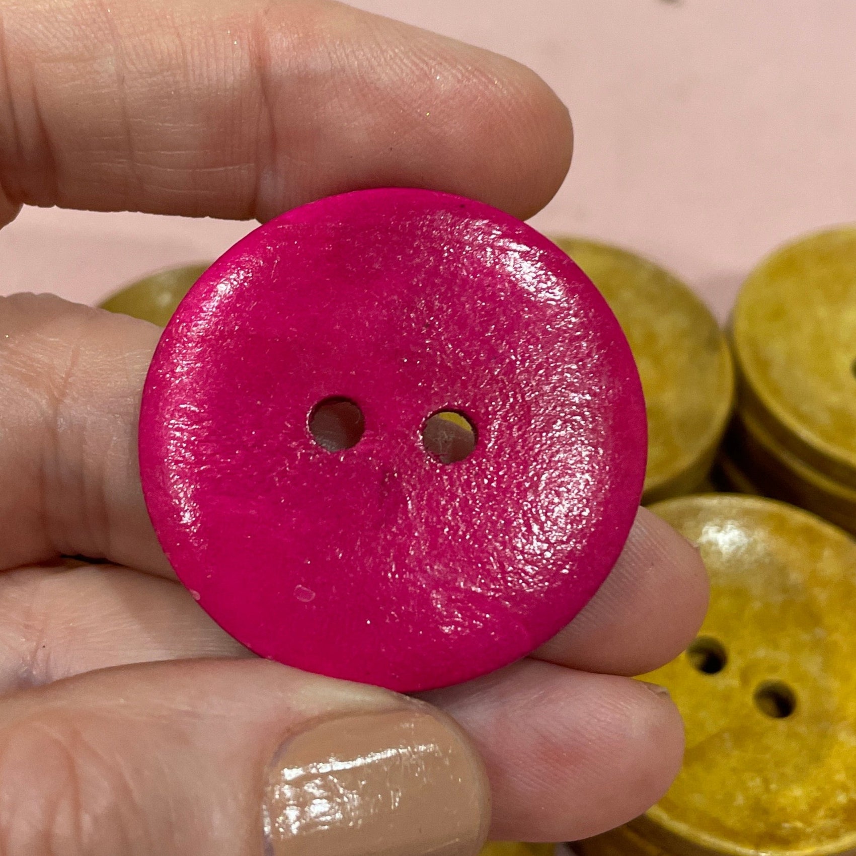 Hand holding a pink button with other buttons on a pink surface
