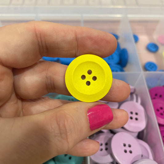 Hand holding a yellow button with a container of colorful buttons in the background