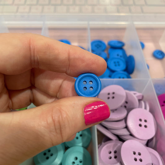Hand holding a blue button with a container of colorful buttons in the background