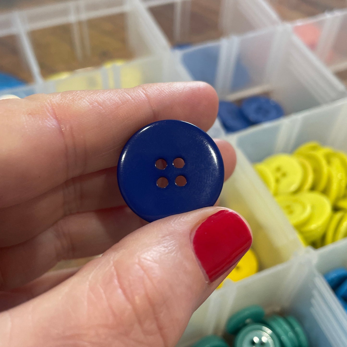 Hand holding a blue button with a container of colorful buttons in the background