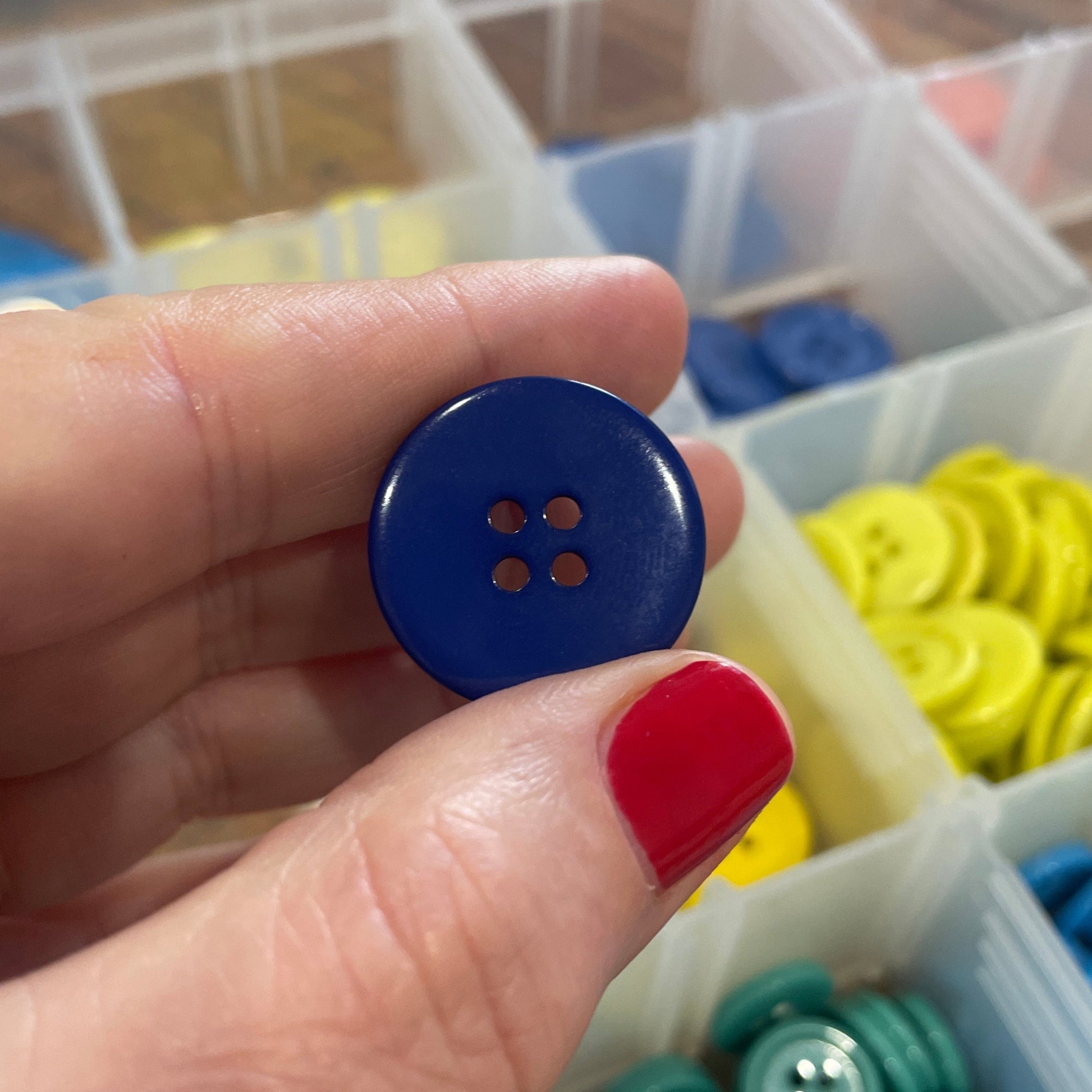 Hand holding a blue button with a container of colorful buttons in the background