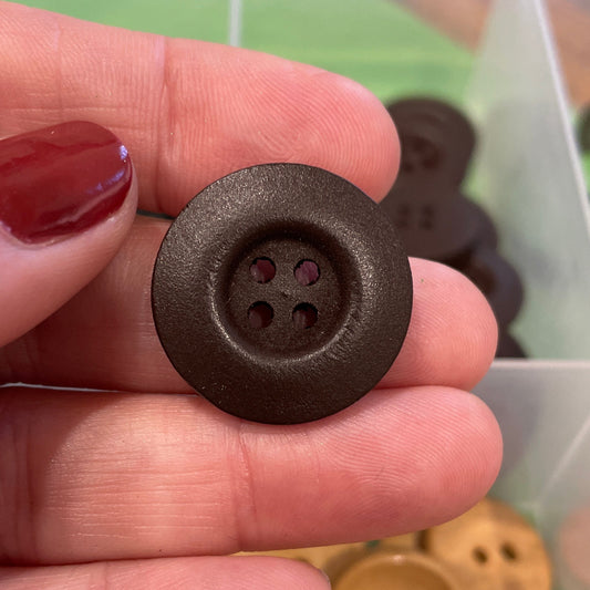 Hand holding a brown button with a container of buttons in the background