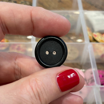 Hand holding a black button with a clear container of buttons in the background