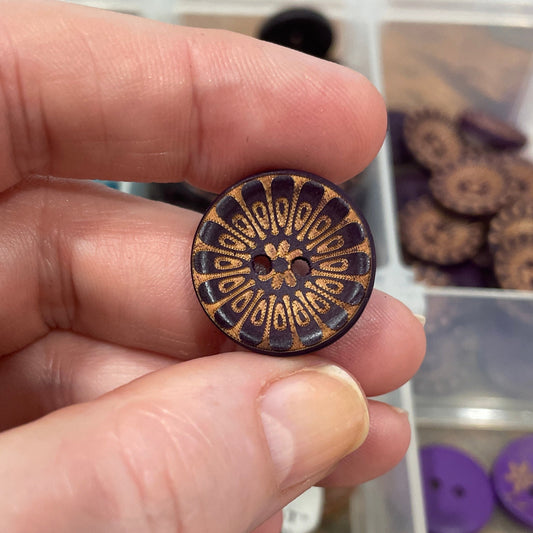 Hand holding a decorative button with a collection of buttons in the background.