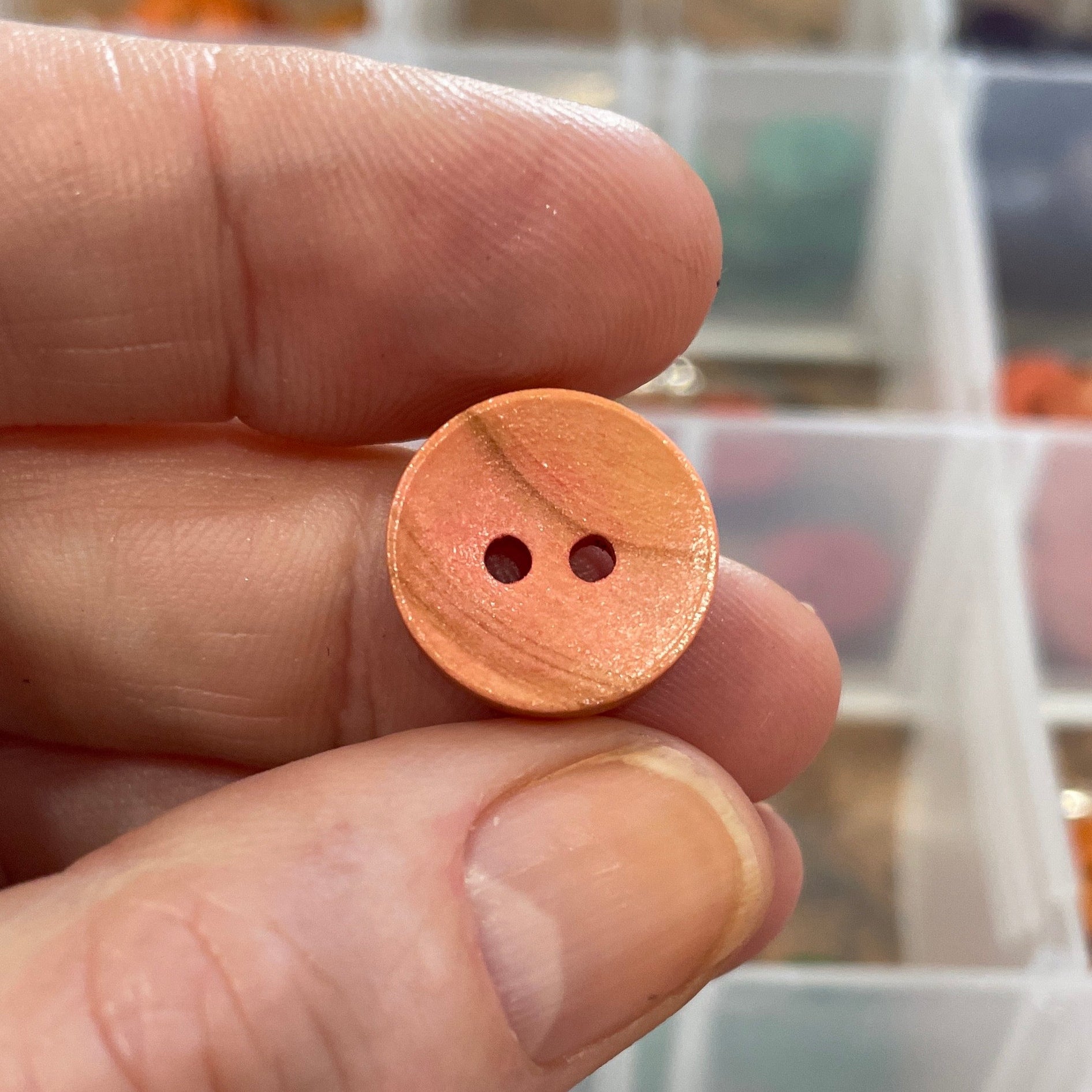 Hand holding a wooden button with a blurred background of button assortment