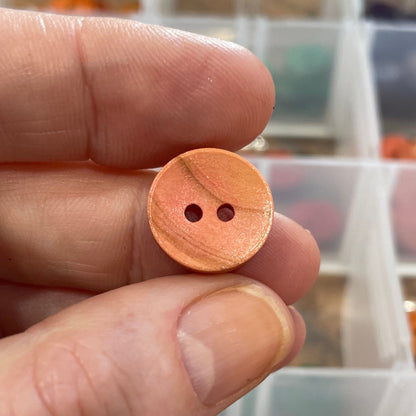 Hand holding a wooden button with a blurred background of button assortment